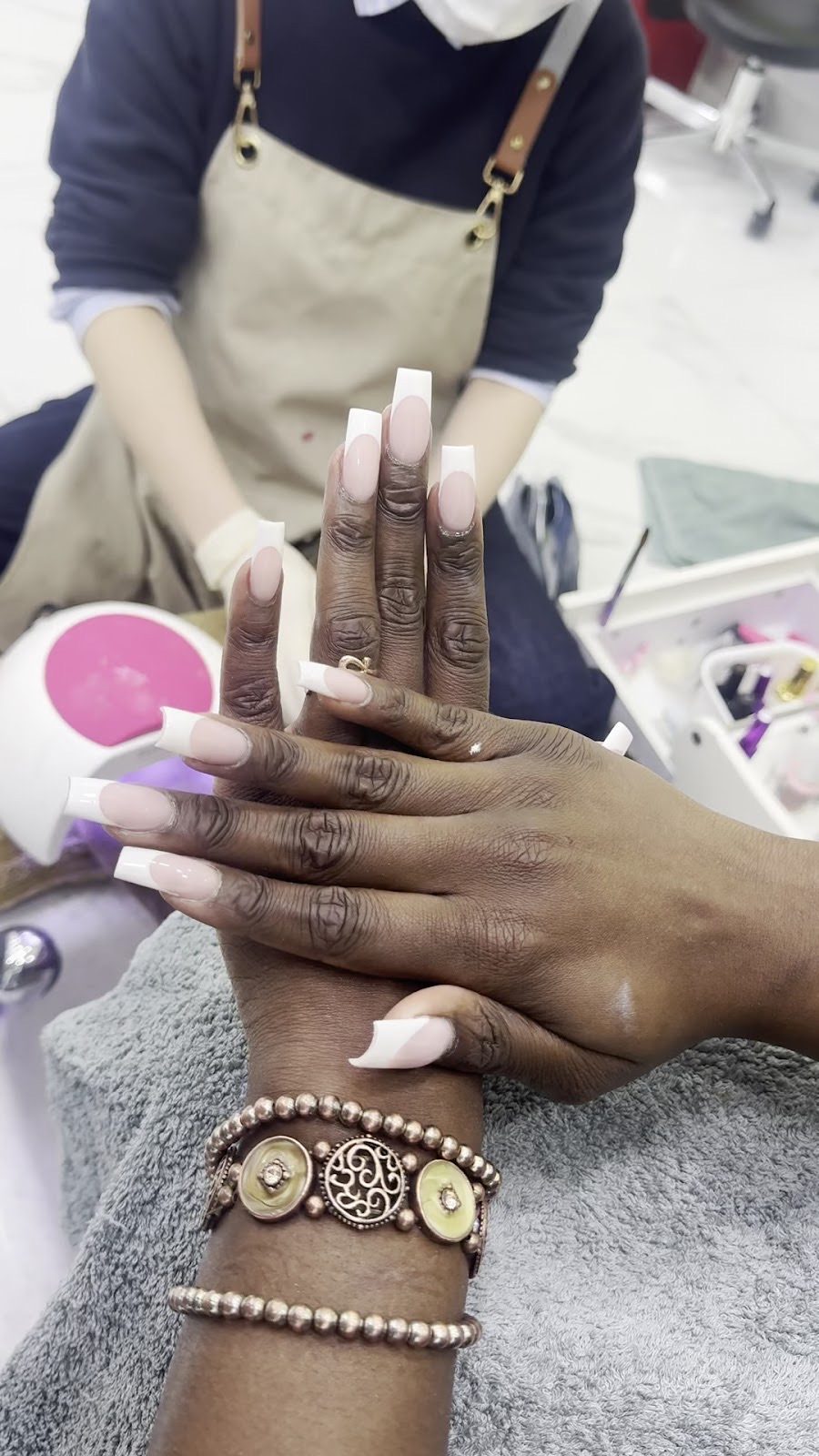 A nail technician in an apron finishing long white-tip nails at the salon desk