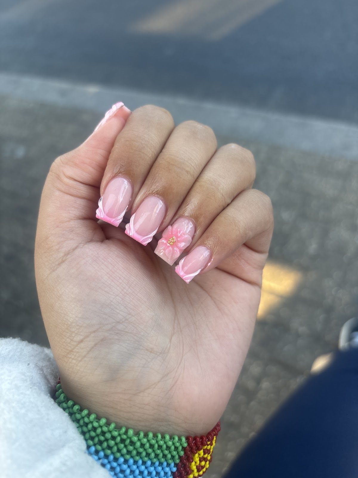 A hand showing short square pink-and-white nails with a floral accent nail
